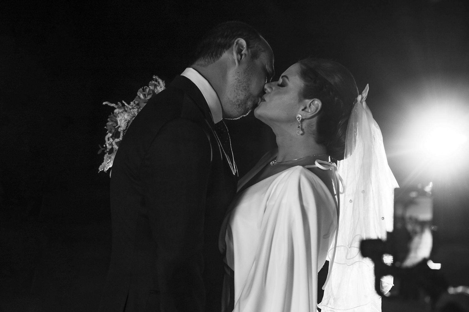 Black and white wedding photo capturing a romantic kiss under spotlight, highlighting love and elegance.