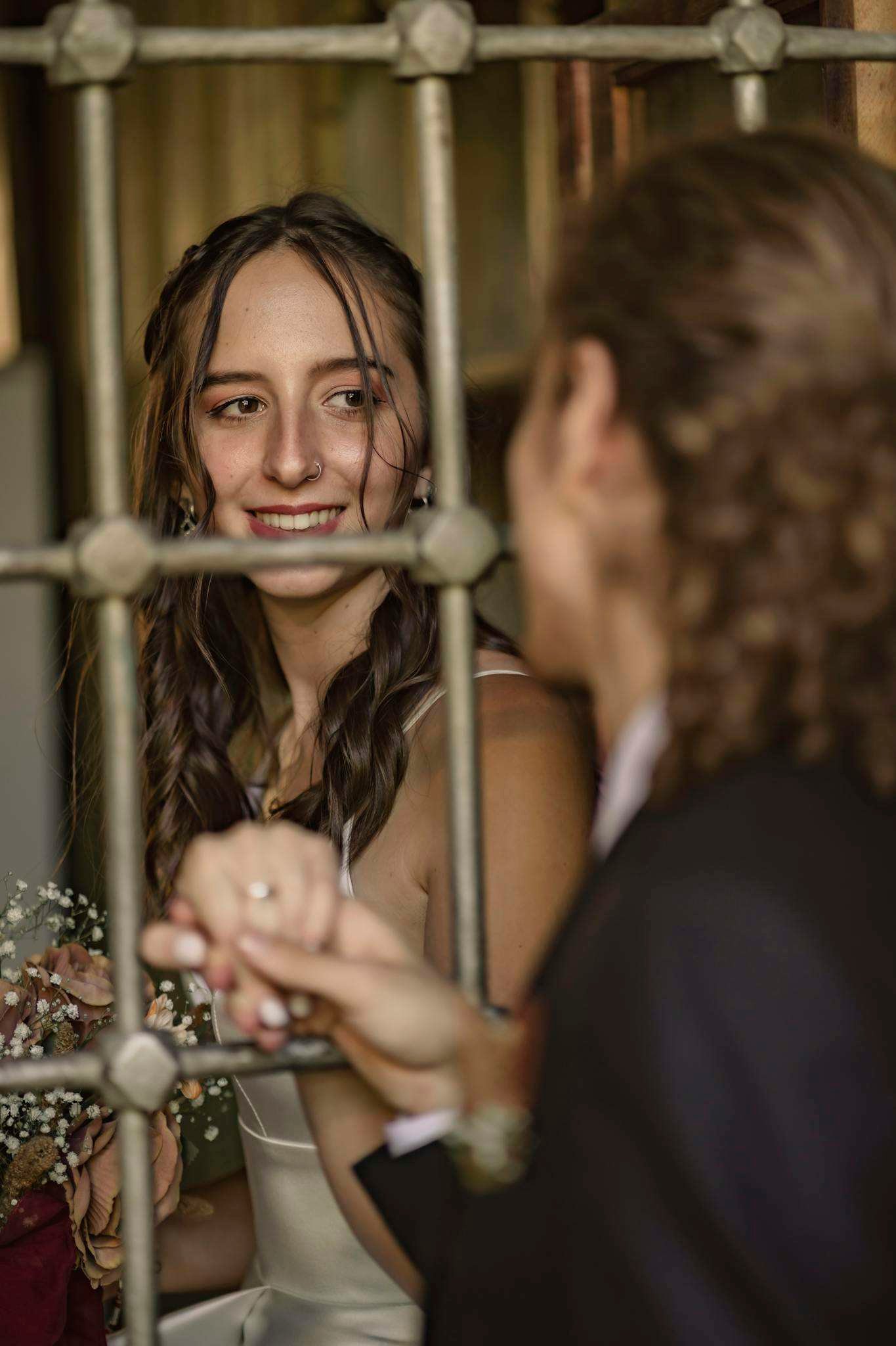 Bride and groom sharing a tender moment through a metal fence on their wedding day.